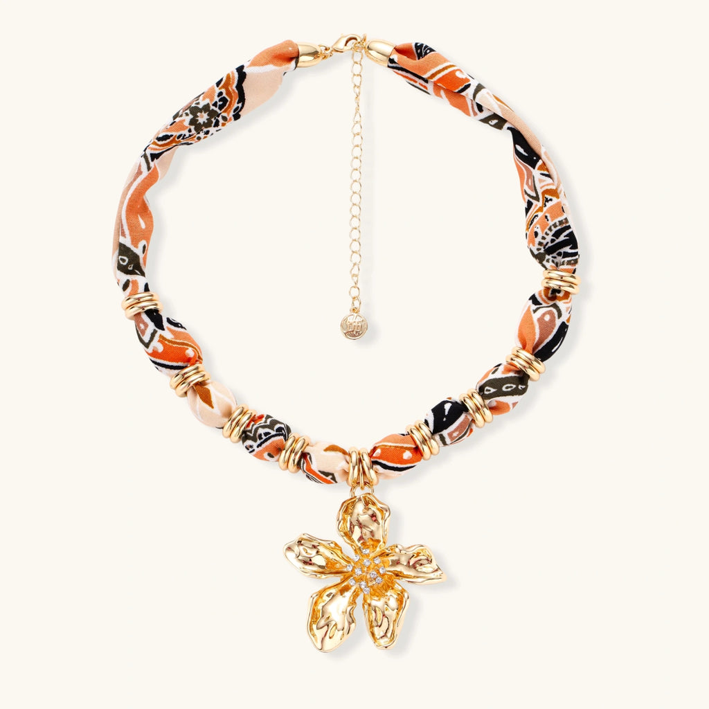 Vibrant patterned fabric necklace with gold-toned flower pendant featuring rhinestone center on white background
