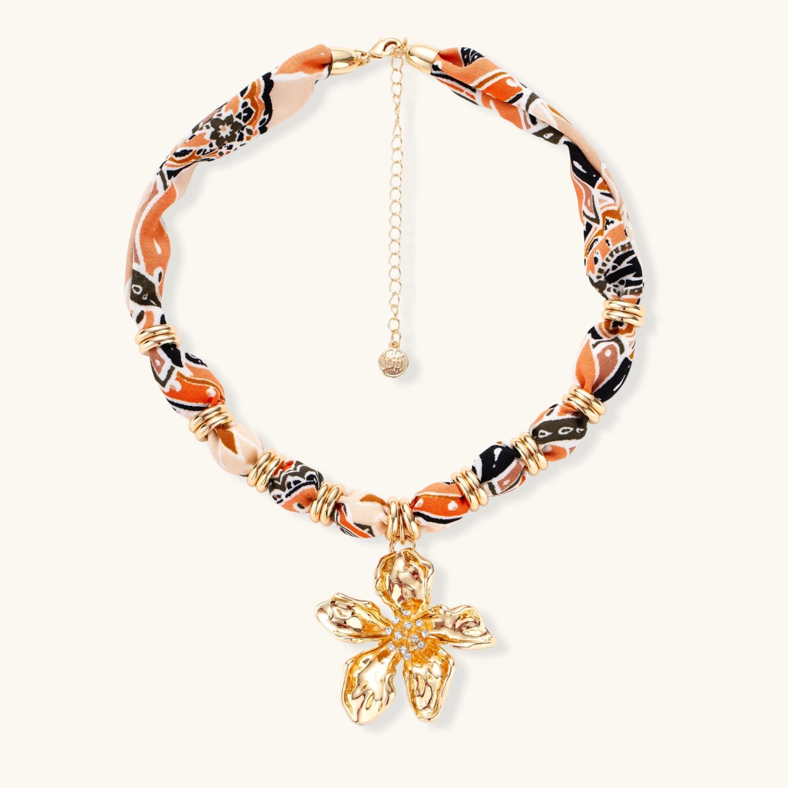 Vibrant patterned fabric necklace with gold-toned flower pendant featuring rhinestone center on white background